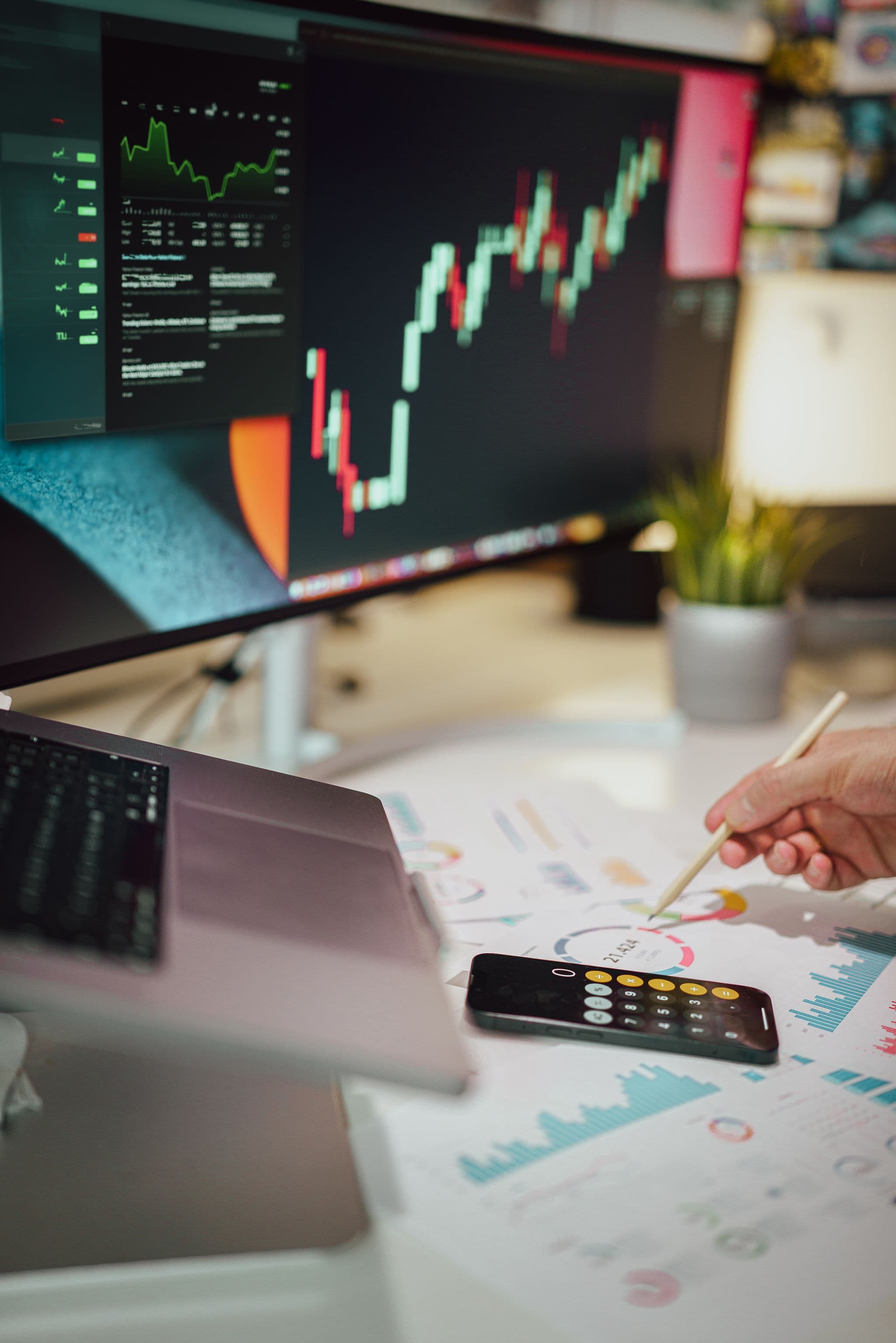 Financial analyst reviewing charts on a desk with a large monitor showing stock market trends.